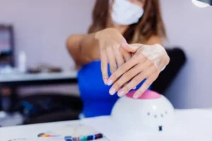 Manicurist wearing a face mask showing manicured hands over a professional UV LED nail lamp.
